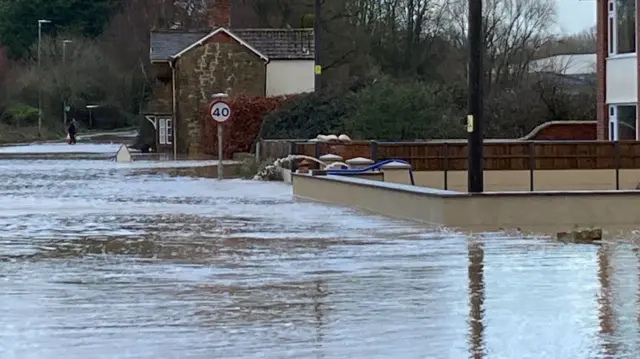 A large area of flood water is seen surrounding a brick home in Ilminster in Somerset. A small blue pump is sending water away from the property