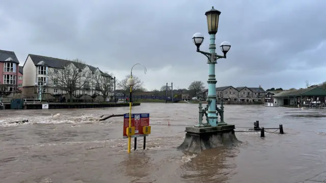 Water bursting over the sides of a riverbank. Items can be seen sticking out of the water