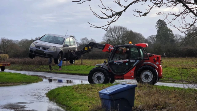 Car being lifted out of flood water by a tractor