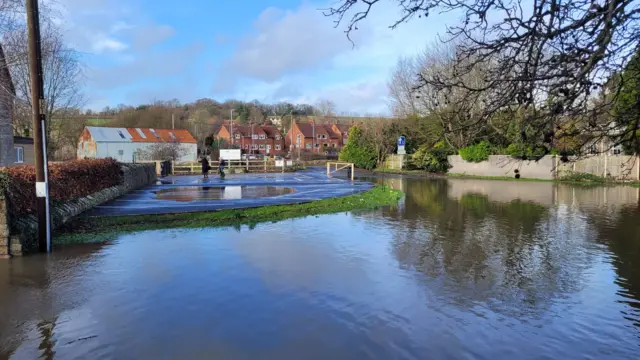 A flooded car park. There are residential properties in the distance.