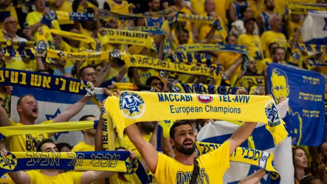 A crowd of people in yellow shirts, holding yellow and blue scarves in the air