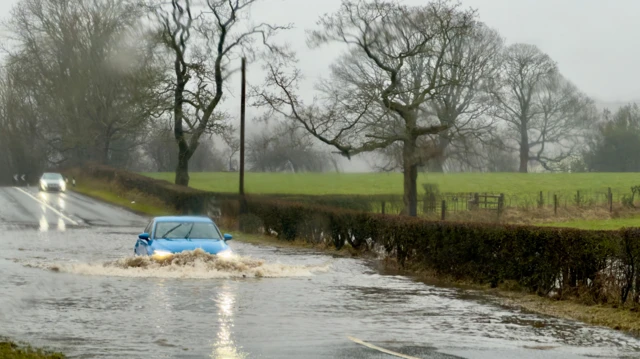 A car drives through flooded water on a road