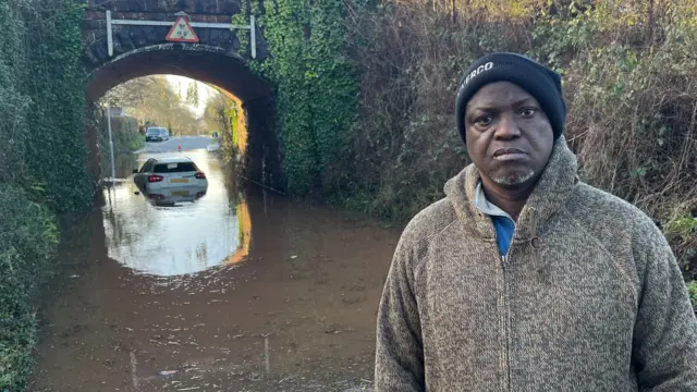 Bartholomew Diaz in front of his car, stuck in flood water in Exeter, Devon