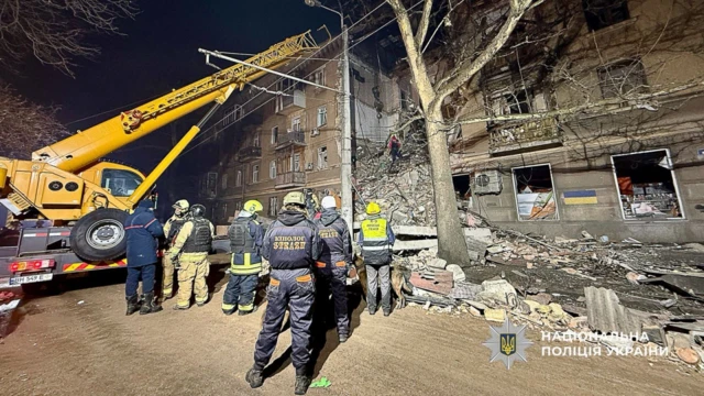 A verified photograph of one of the badly damaged buildings in Odesa - emergency workers look on as a crane is being used on the debris