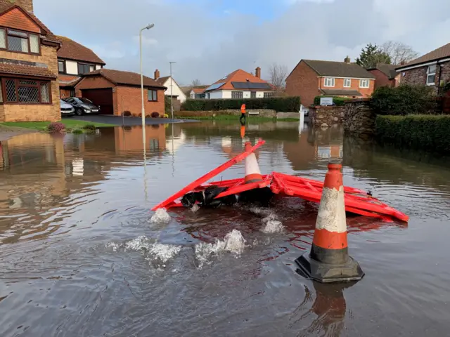High levels of floodwater in a residential street in Taunton. In the front of the frame is some red cones which have turned over in the water