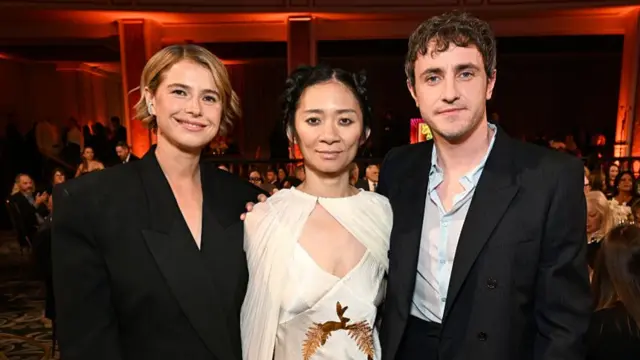 Chloé Zhao, centre, stands with Jessie Buckley and Paul Mescal on either side of her - she wears a cream dress with cape detail and embroidery of rabbits and ferns - Buckley and Mescal wear dark suit jackets