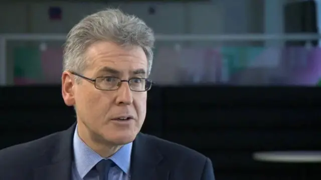 A man with grey hair and glasses in a blue suit