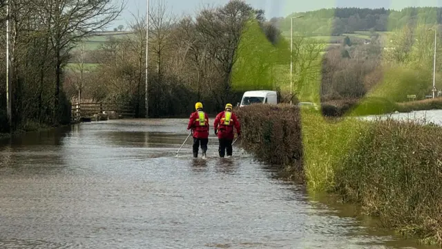 Firefighters walk through floodwater to help a vehicle stuck in the water
