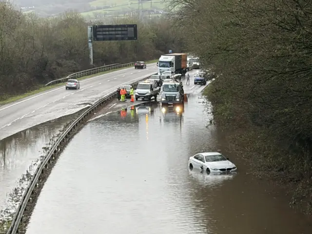 A white car submerged in flood water on a main A-road in Devon