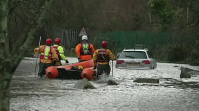 Firefighters moving through flood water with dinghy to driver trapped in car during floods