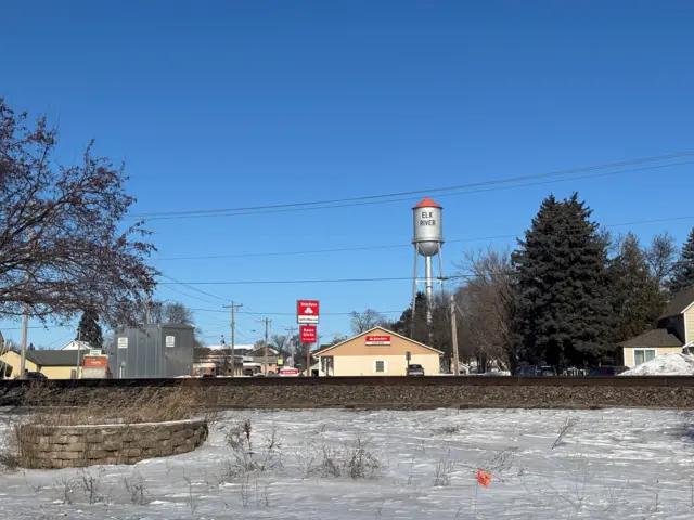 A snow-covered field in the foreground with a water town in the background with the words Elk River.
