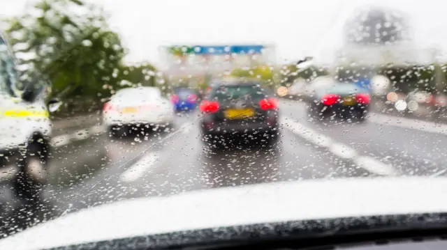A photo looking out the front window of a car on a busy road. It is difficult to see out of the window due to heavy rain. There are four other vehicles on the road.