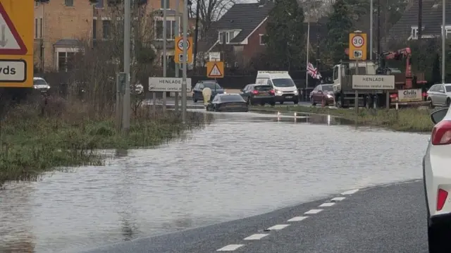 A flooded road on the outskirts of Taunton. The road is submerged and cars that have stopped are visitl