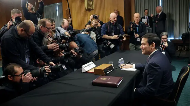Marco Rubio facing cameras and press sat behind a table in the Senate.