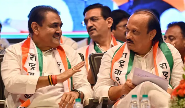 Ajit Pawar and Praful Patel seen sitting together, wearing white kurtas and tricolour sash with the party name on it
