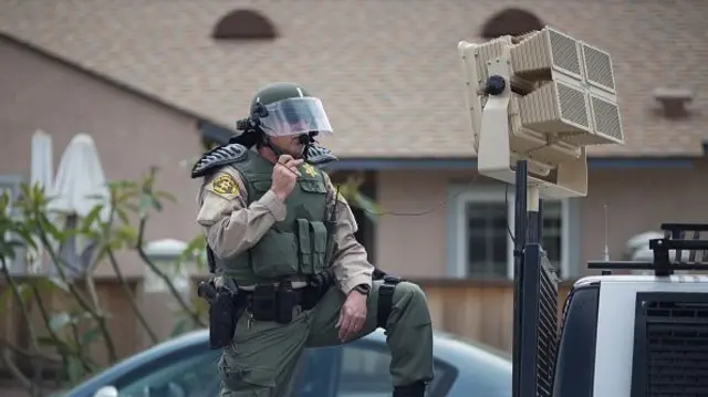 A man wearing riot gear stands ready to use a LRAD