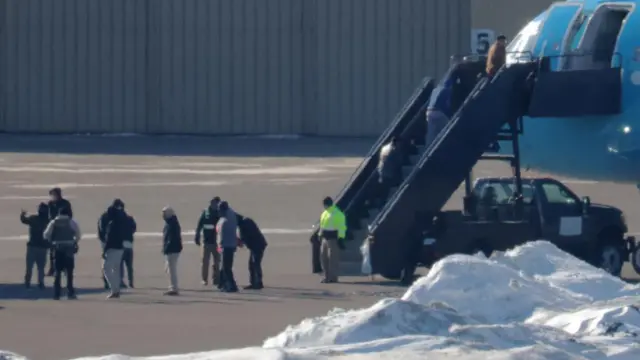 line of people standing on tarmac to board a flight of stairs up to a plane