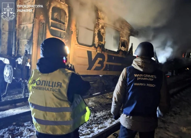 A war crime prosecutor and a police officer work next to a passenger train hit by a Russian drone strike, amid Russia's attack on Ukraine, in Kharkiv region