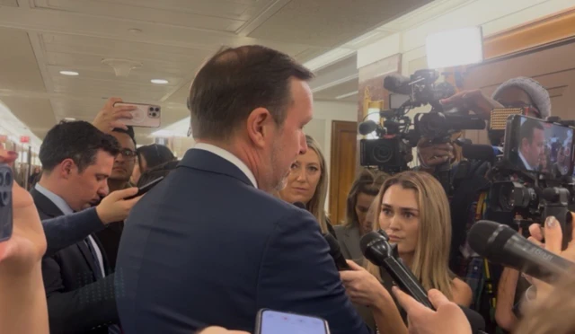 Democratic Senator Chris Murphy outside Senate hearing room, people holding microphones up to him.