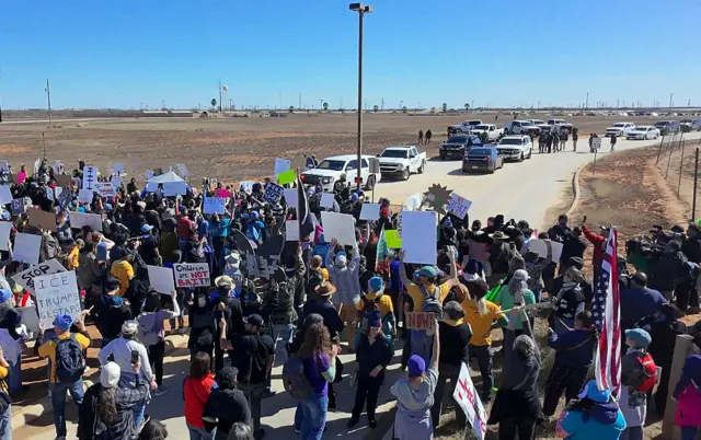 above shot of dozens of protesters gathered on a desert road in front of officers' vehicles