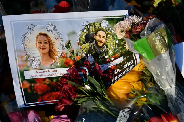 A card with images of Renée Good and Alex Pretti lies among flowers and other mementos at a memorial in Minneapolis, Minnesota