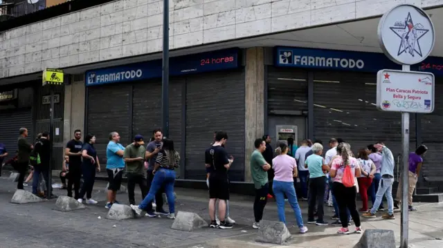 People queue in front of a pharmacy in Caracas following the US strike