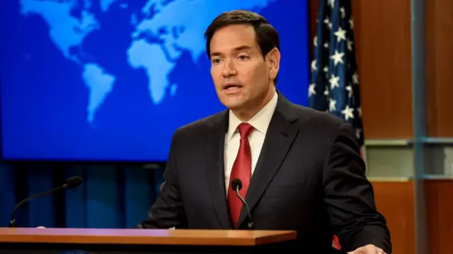 Marco Rubio trong bộ vest và cà vạt đang phát biểu trên bục giảng.