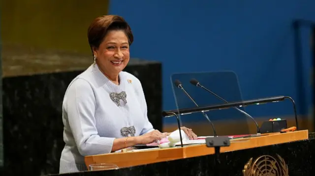 Bà Kamla Persad-Bissessa tại Liên Hợp Quốc năm ngoái. Bà đang đứng trước bục phát biểu và nói vào micro. Trong ảnh, bà đang mỉm cười.