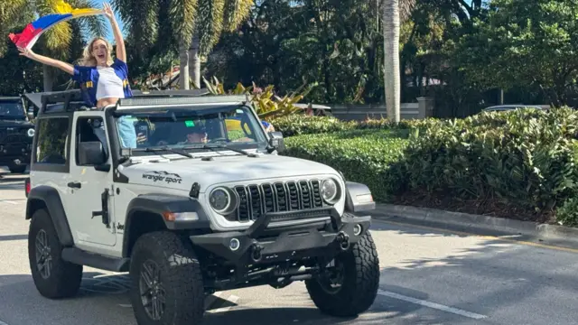 Image of woman standing through sunroof of car, waving Venezuelan glag