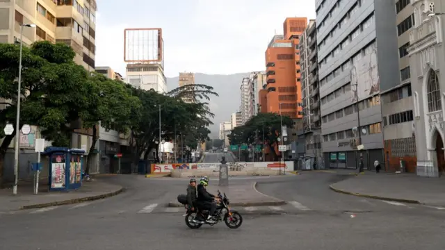 People ride a motorbike on an empty street in Caracas