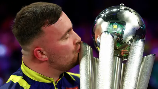 Luke Littler kisses the trophy