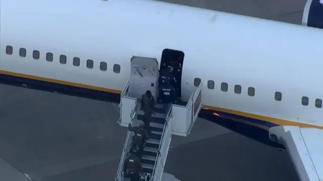A plane with stairs attached and FBI agents walking aboard