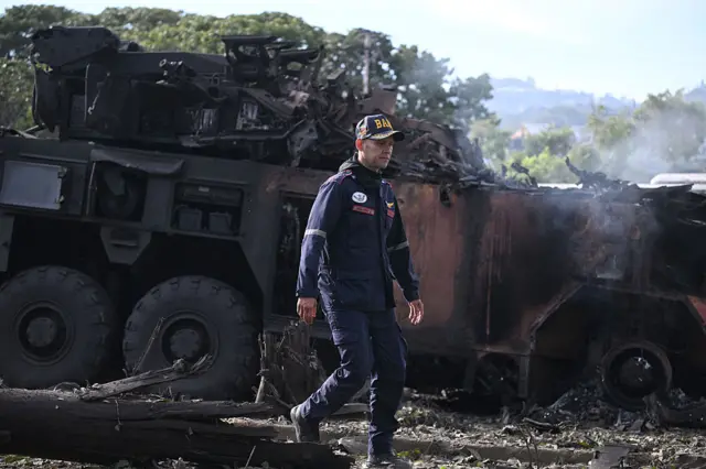 A firefighter passes by a burnt military vehicle at La Carlota air base in Caracas