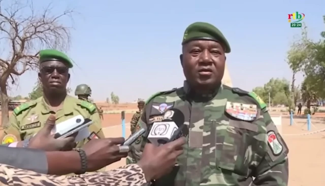 General Abdourahamane Tiani in military figures speaking to reporters who are holding microphones in front of him
