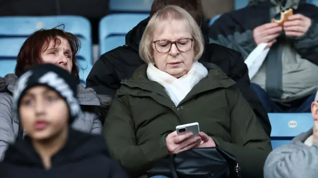 A Leicester fan checks her phone before kick-off