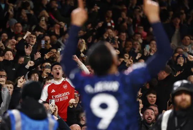 Arsenal fans cheer as Jesus celebrates his goal in the foreground