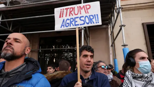 A man holds a placard reading "Trump the aggressor" as demonstrators protest outside the U.S. Embassy in Madrid against the US strike on Venezuela