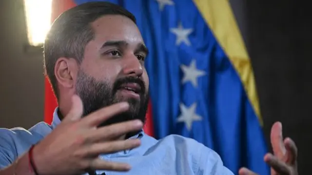 Maduro Guerra sits in front of a Venezuelan flag
