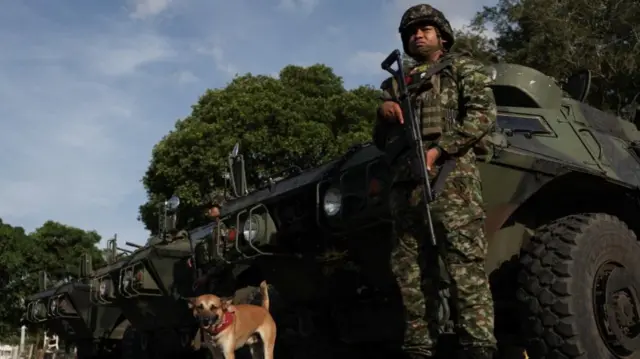 A soldier with a gun stands by a tank