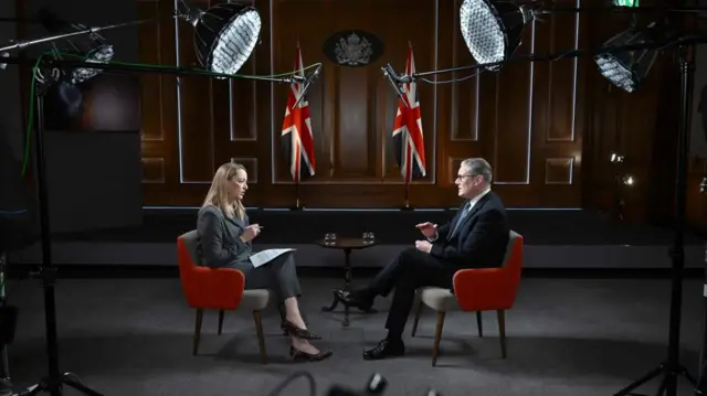 Laura Kuenssberg interviewing Keir Starmer, they are sat on red chairs with TV lights and microphones visible over their heads