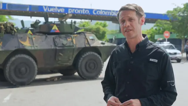 Will Grant stands in front of a tank at the border of Colombia and Venezuela