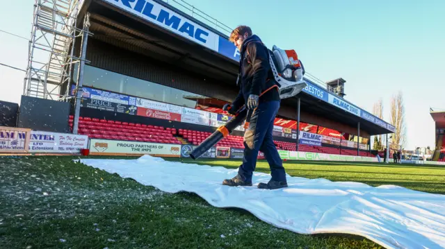 Groundsman uses a leaf blower to clear snow and ice from a pitch cover