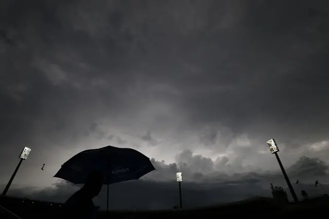 A fan with an umbrella stands under dark skies at the SCG