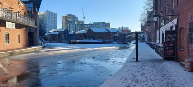 A canal is covered in ice while a footpath running along the water way is coated in snow