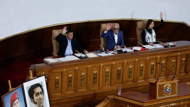 Three people - the assembly president, first vice president, and second vice president - sit at a large wooden desk at the National Assembly