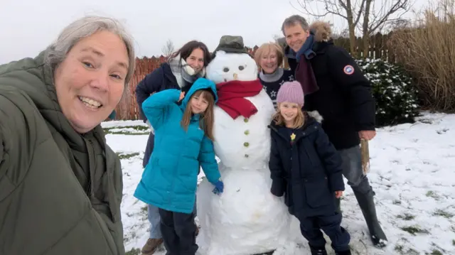A family stands with a snowman and takes a selfie
