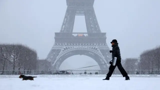 A woman walks her dog in a snow-covered area in front the Eiffel Tower, as winter weather with snow and cold temperatures hits a large part of the country, France, January 5, 2026.