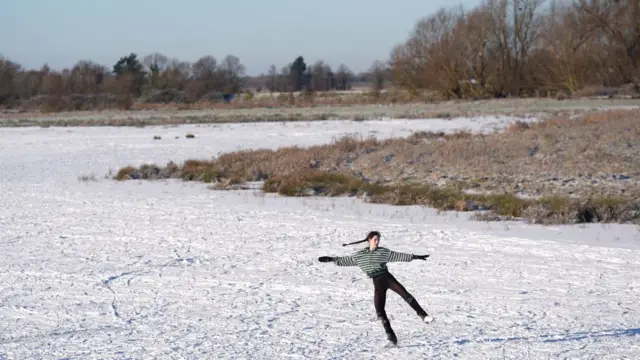 A woman wearing a striped green top skates on a frozen over field