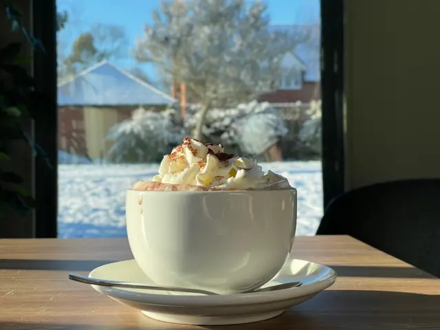 A hot chocolate in front of a snowy garden