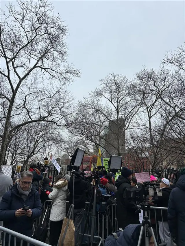 A photo of individuals gathered outside court. Some can be seen holding signs and flags